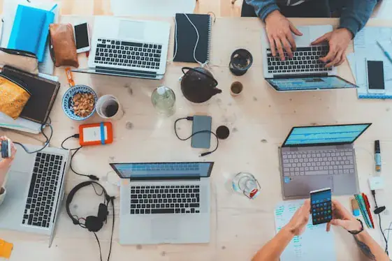Team working across laptops and phones around a shared desk